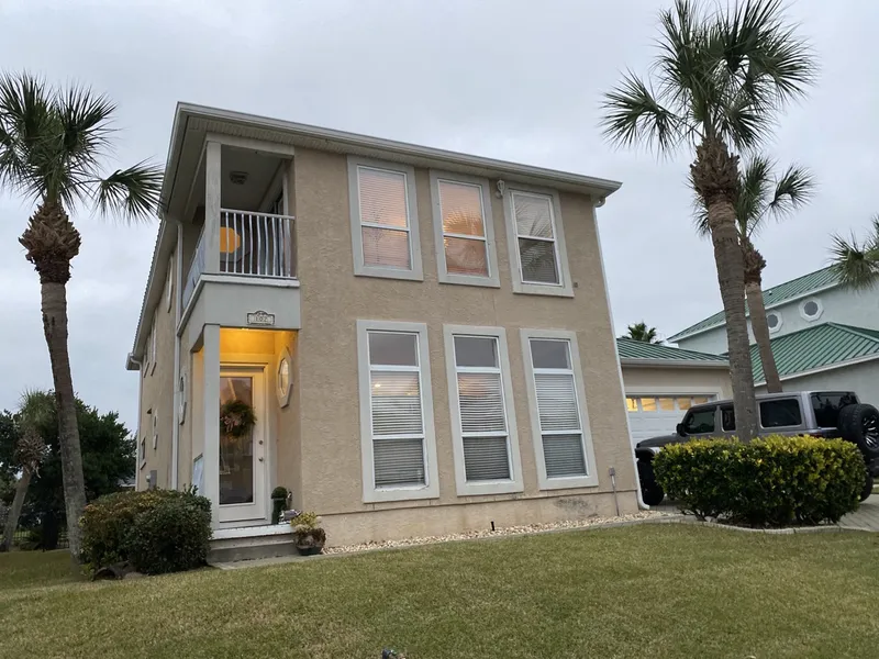 The house before renovation, clad in tan stucco with aluminum-framed windows and a small second-floor balcony.