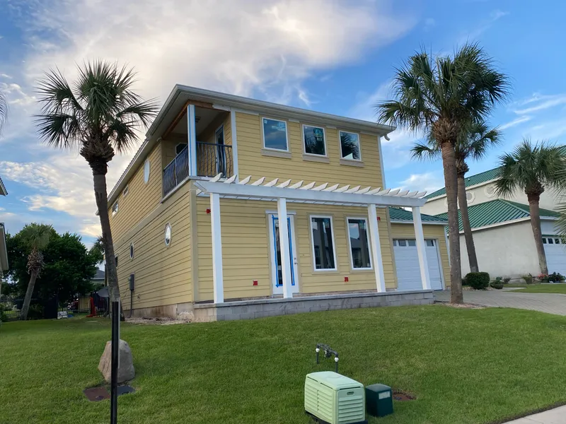 The house with new lap siding installed and painted yellow, a white pergola over the new front porch, and new windows in place.