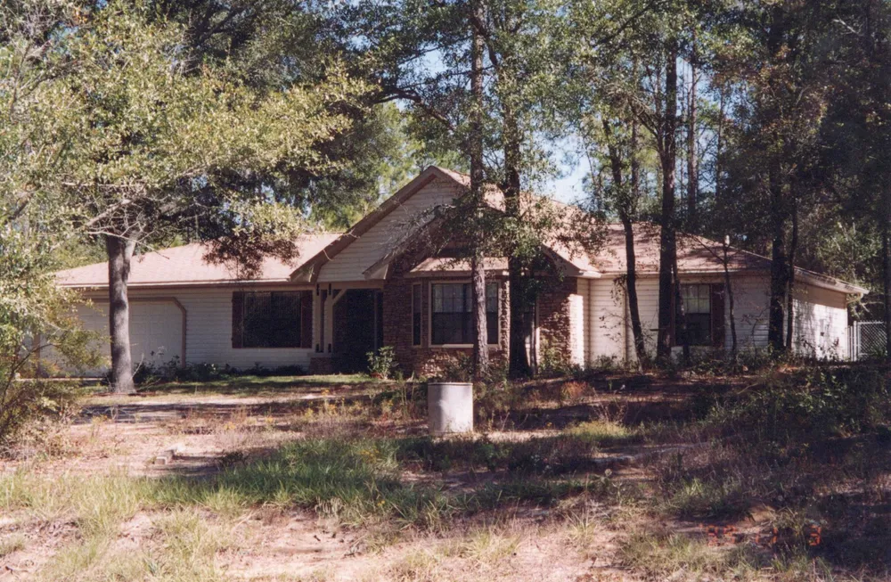 A single-story house with a stone-faced entry and bay window on a wooded lot.