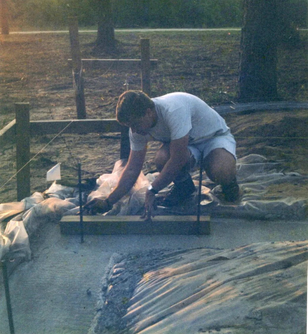 Guy Garrett as a young man, kneeling at a foundation with batter boards and string lines set up behind him.