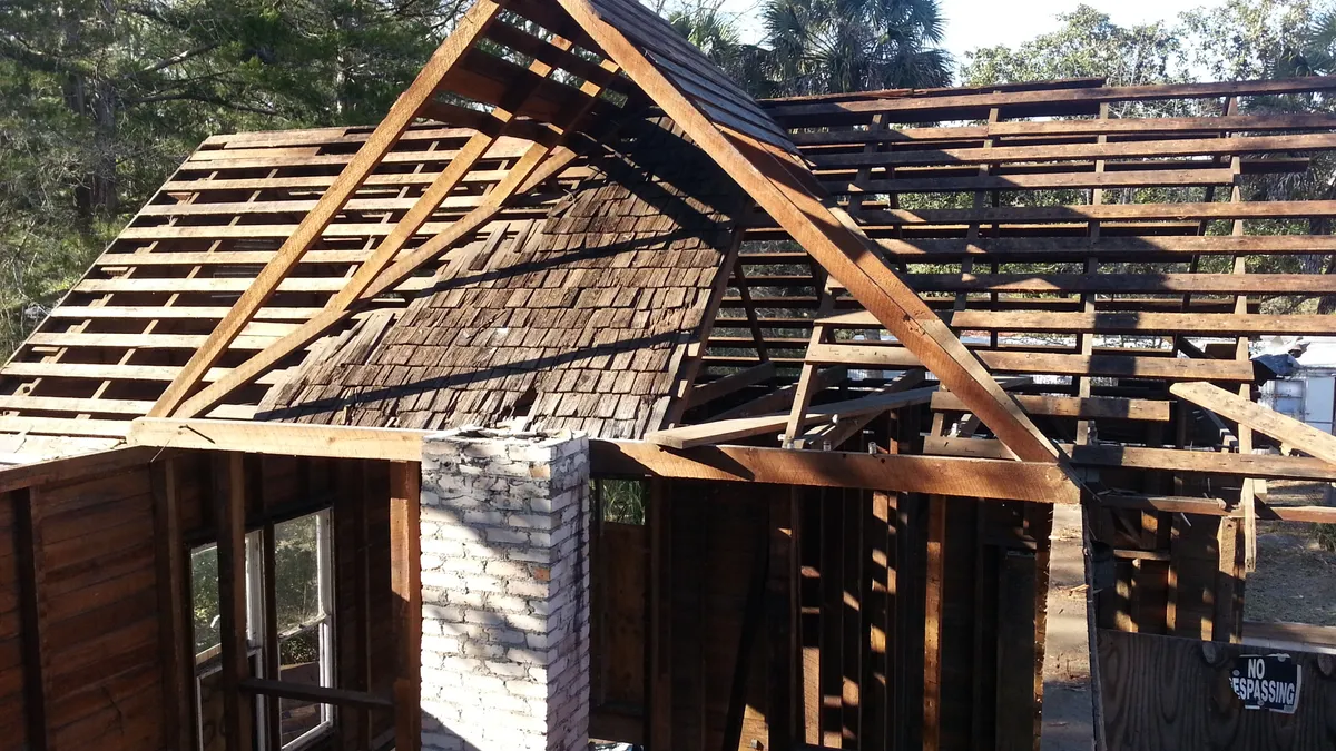 Exposed timber roof framing and wood shingles around a brick chimney.
