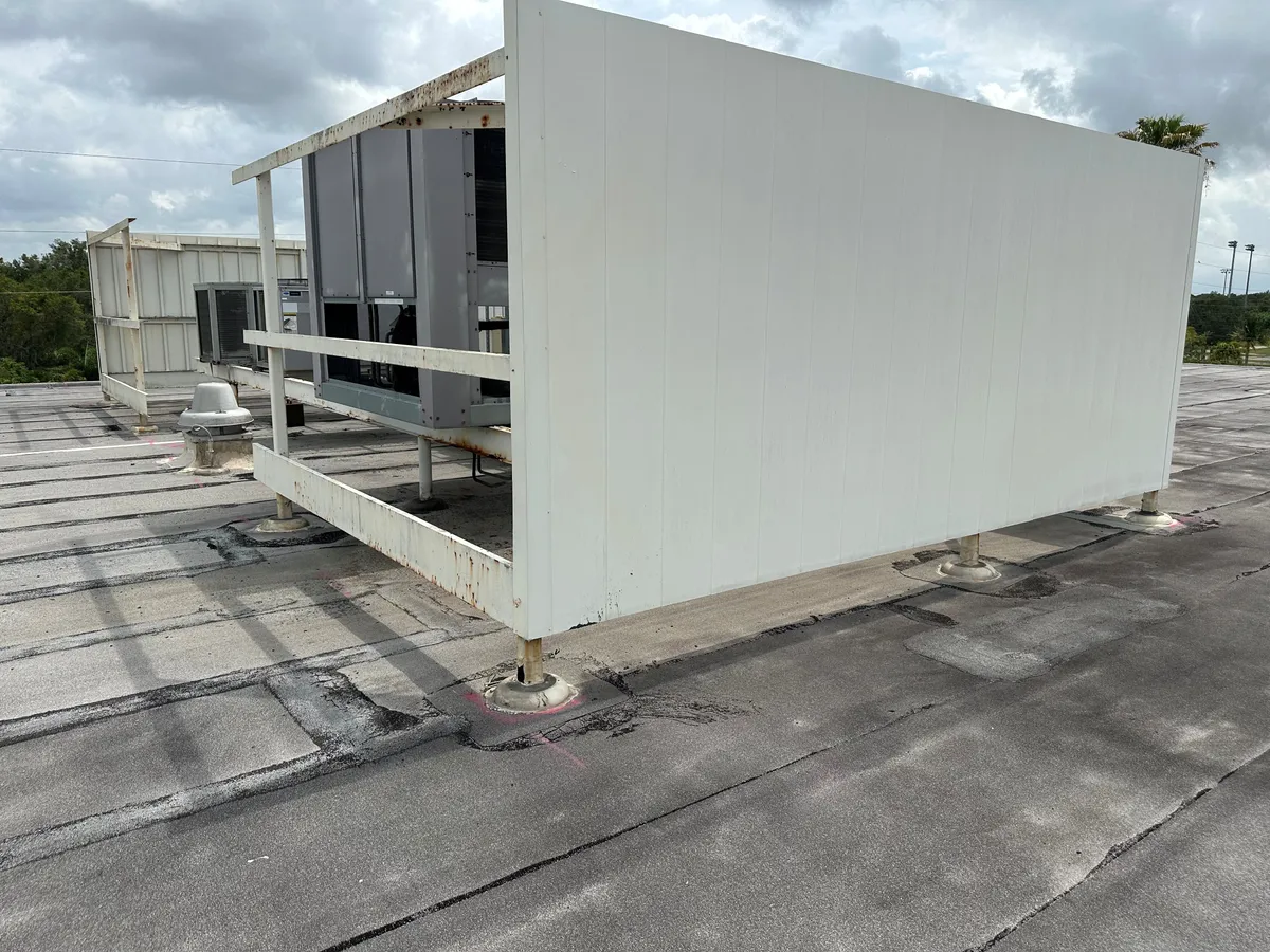 Rooftop equipment on raised steel supports behind a screen wall, on the existing roof surface.
