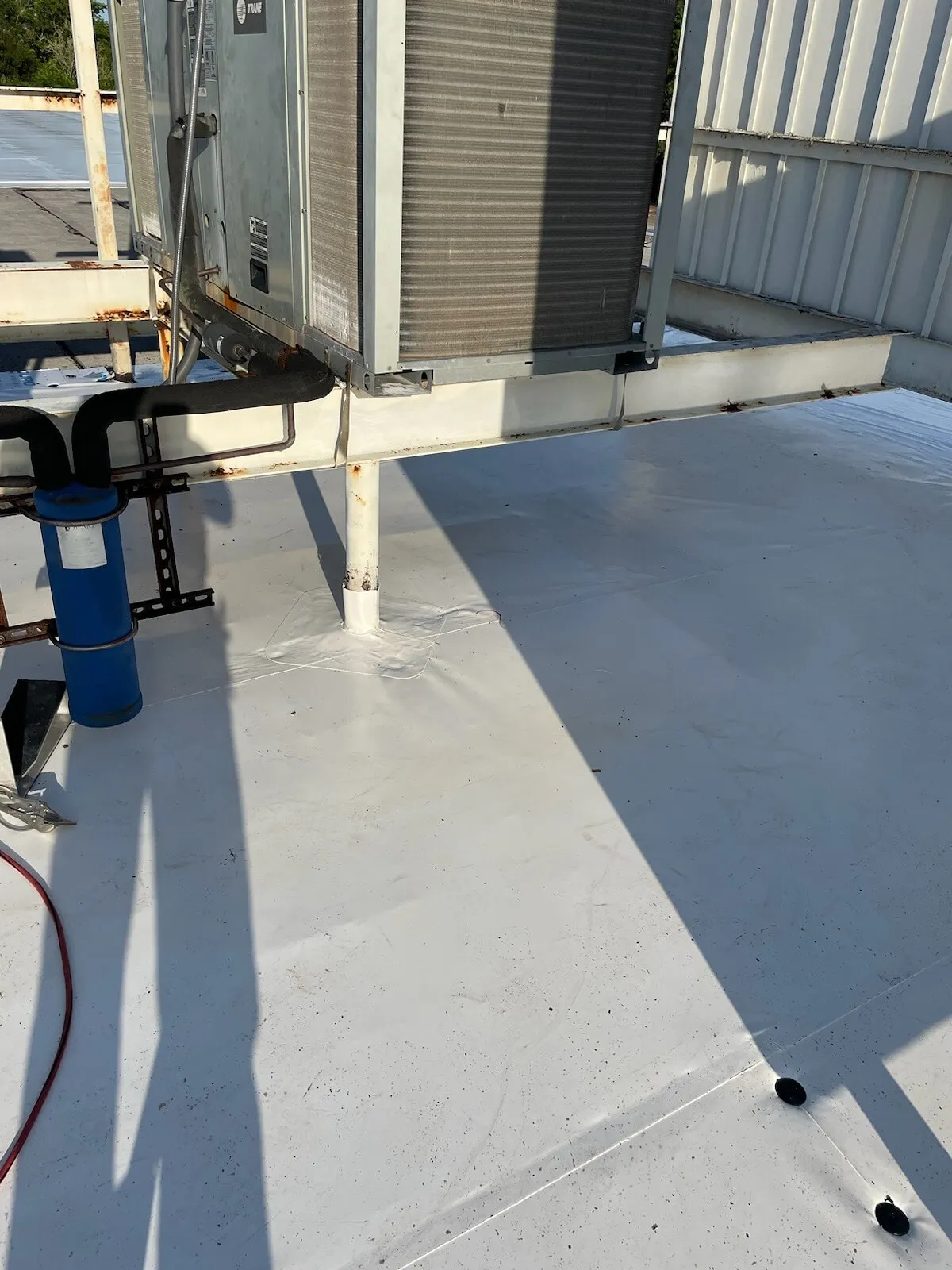 White membrane around the legs of raised rooftop equipment, with a cord and fittings nearby.