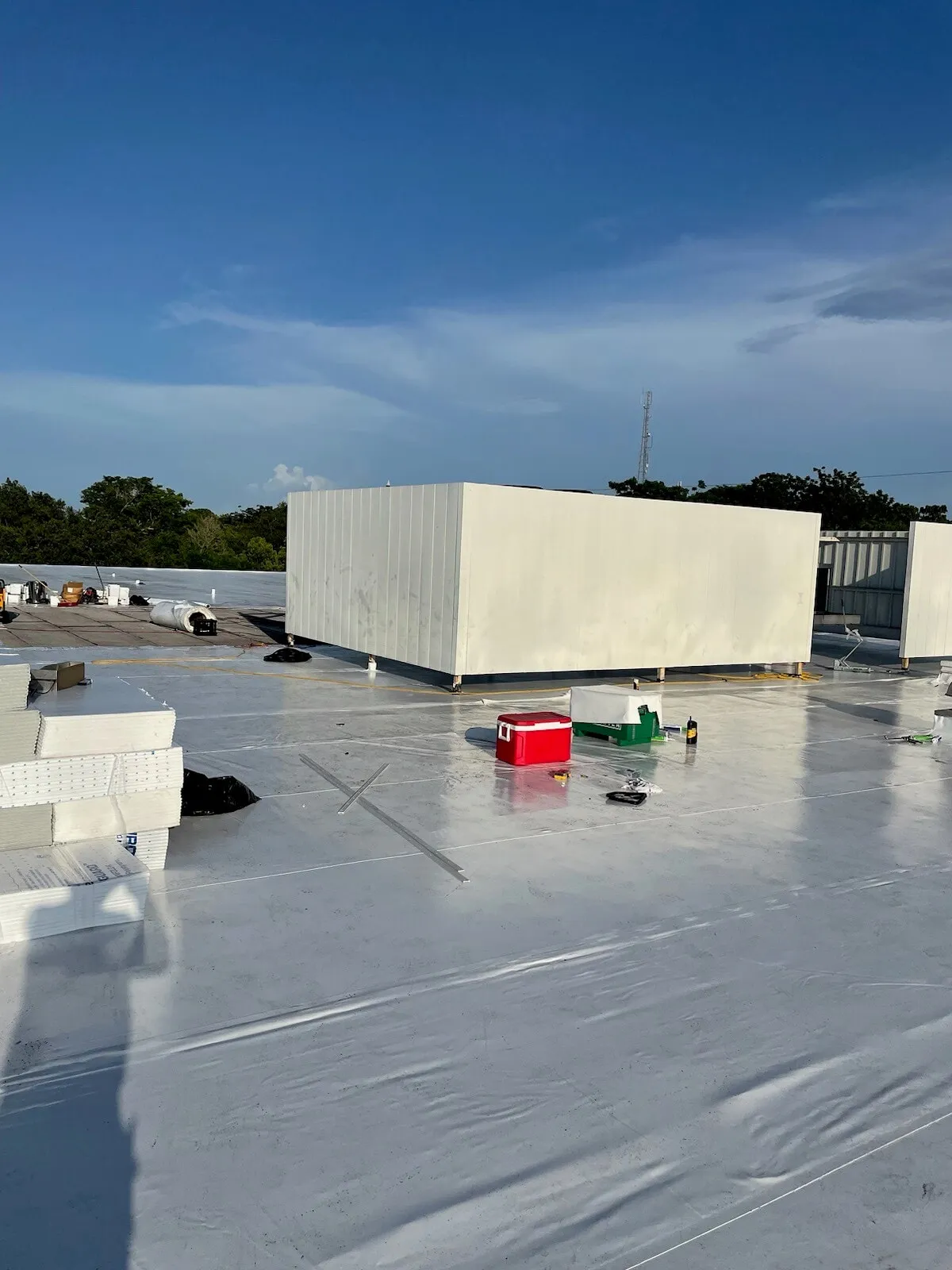 White membrane across the roof in daylight, with an equipment enclosure, tools, and materials still in place.