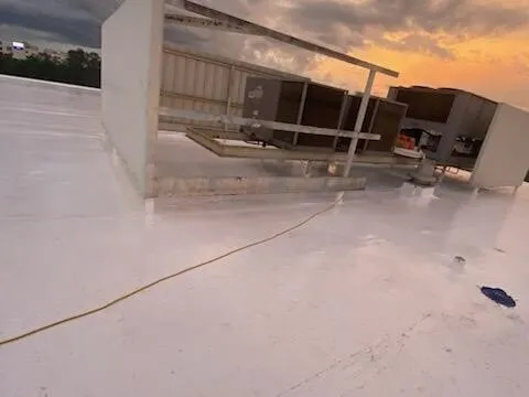 White membrane beside rooftop equipment and its screen at dusk, with a cord running across the roof.