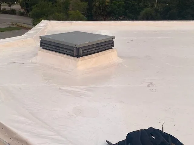 White membrane wrapped up the sides of a raised vent curb, with a tool bag on the roof.