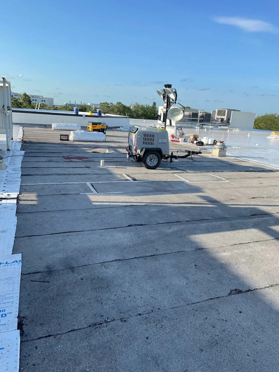 Existing roof area with a portable light tower and equipment staged, and new membrane visible at the far edge.