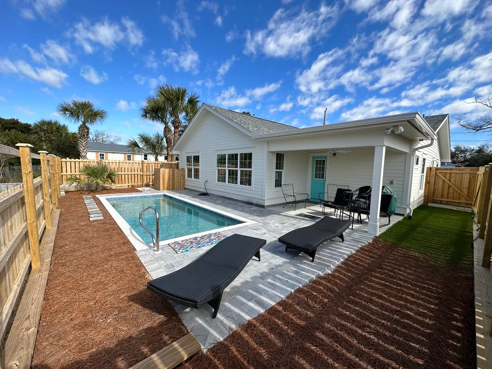 White-sided home addition and covered porch beside a pool and paved patio.