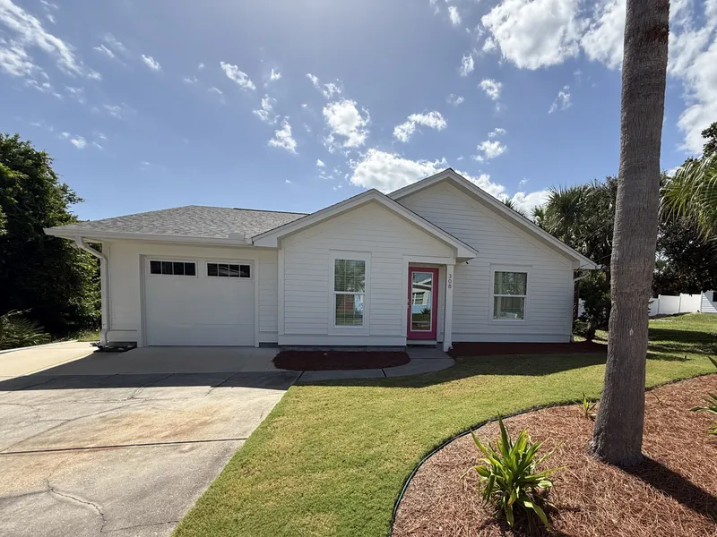 Completed white-sided house with a garage, pink front door, lawn, and landscaped beds.