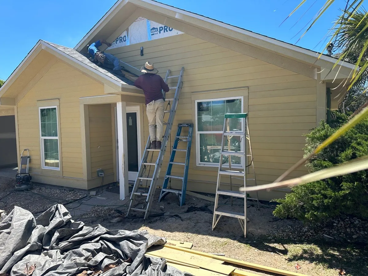 Crew members installing upper gable siding using ladders and the porch roof.