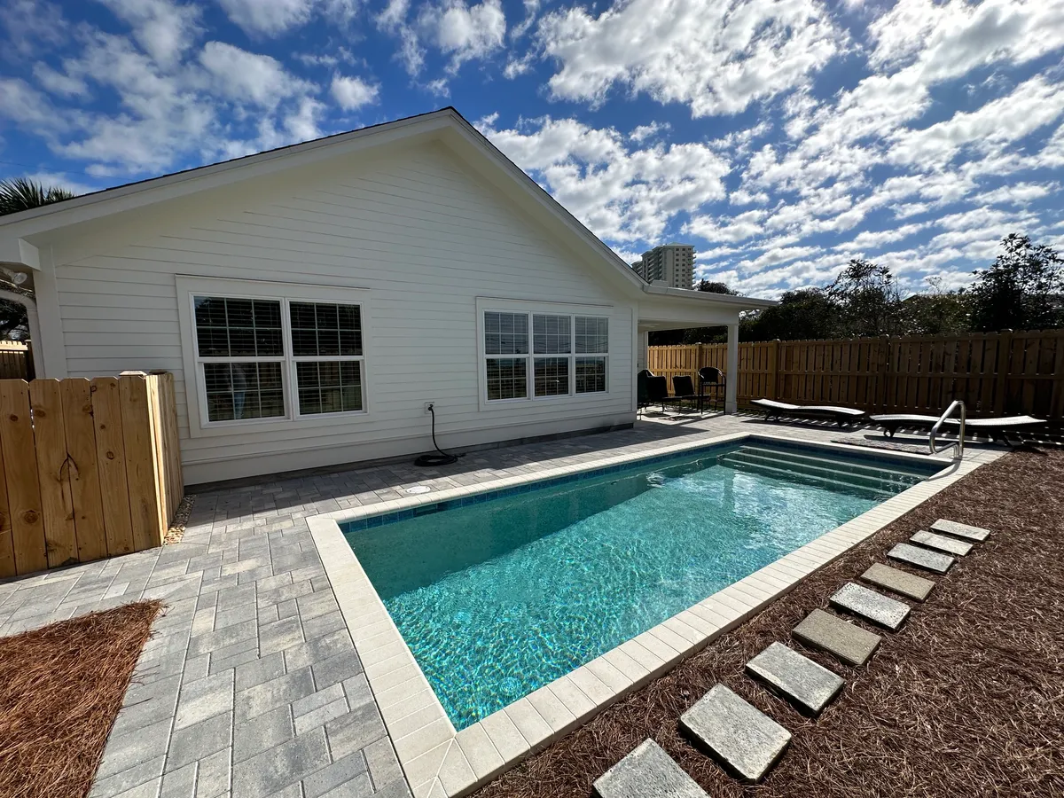 Completed white-sided addition with large windows viewed across the backyard pool.