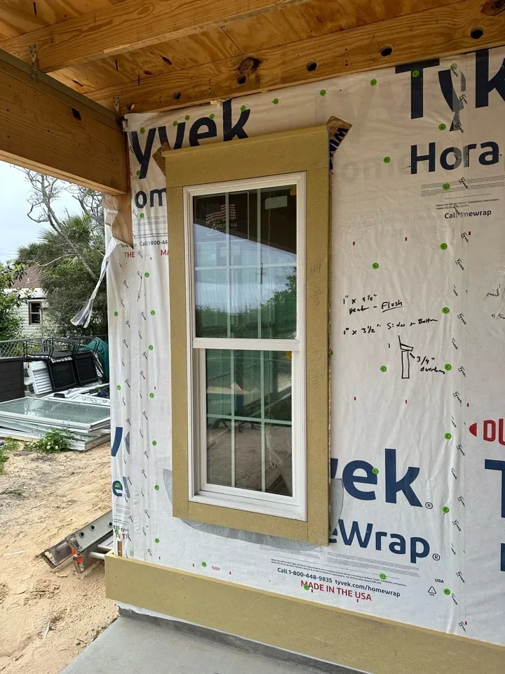 Installed window and exterior trim surrounded by housewrap during construction.