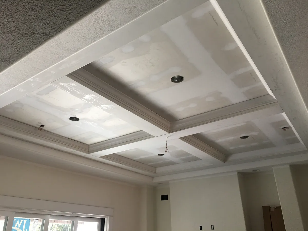 Coffered ceiling beams and crown molding with drywall patches still unpainted, before final finishing.