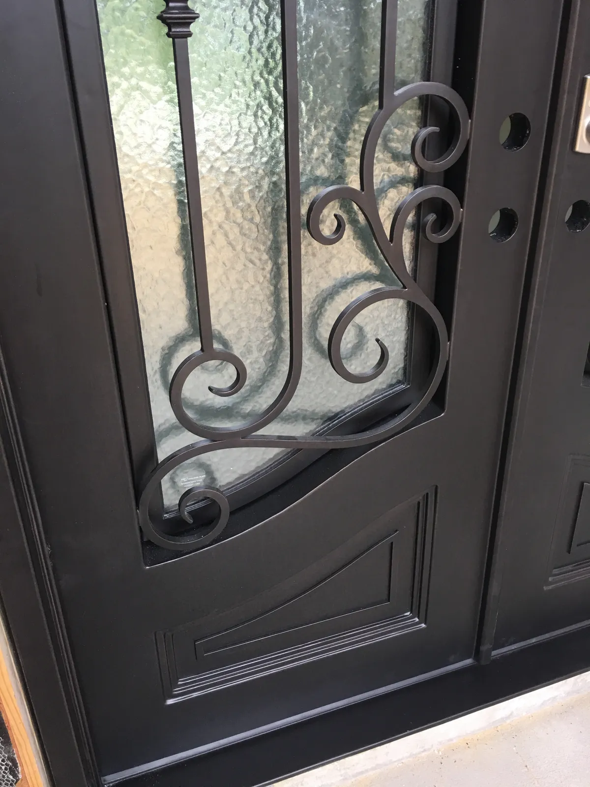 Close view of an entry door's textured glass panel and scrolled metalwork.