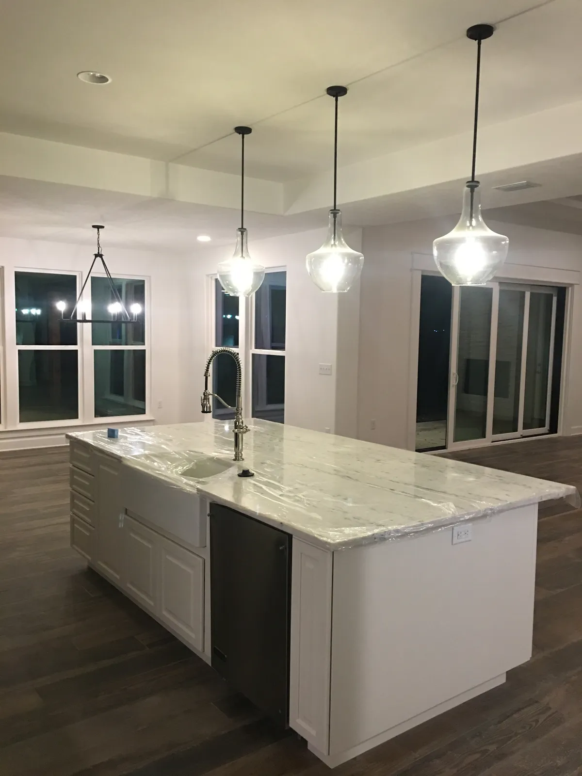 Kitchen island with its countertop still under protective film and pendant lights, looking toward the dining area's trimmed windows and sliding doors.