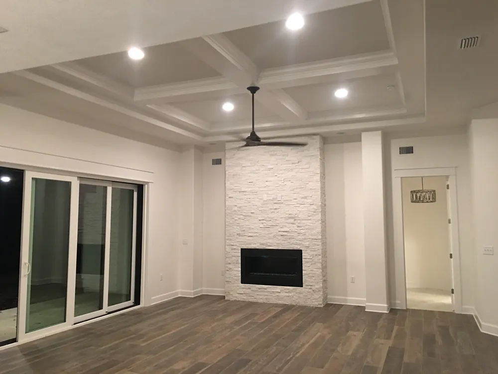 Living room with a coffered ceiling and crown molding, a stacked-stone fireplace wall, sliding glass doors, and trimmed doorways.