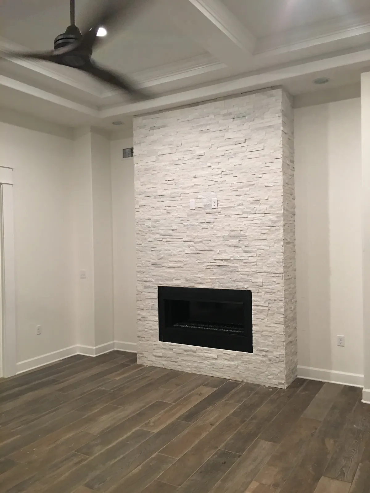 Stacked-stone fireplace wall beneath the coffered ceiling, with trimmed openings on either side.