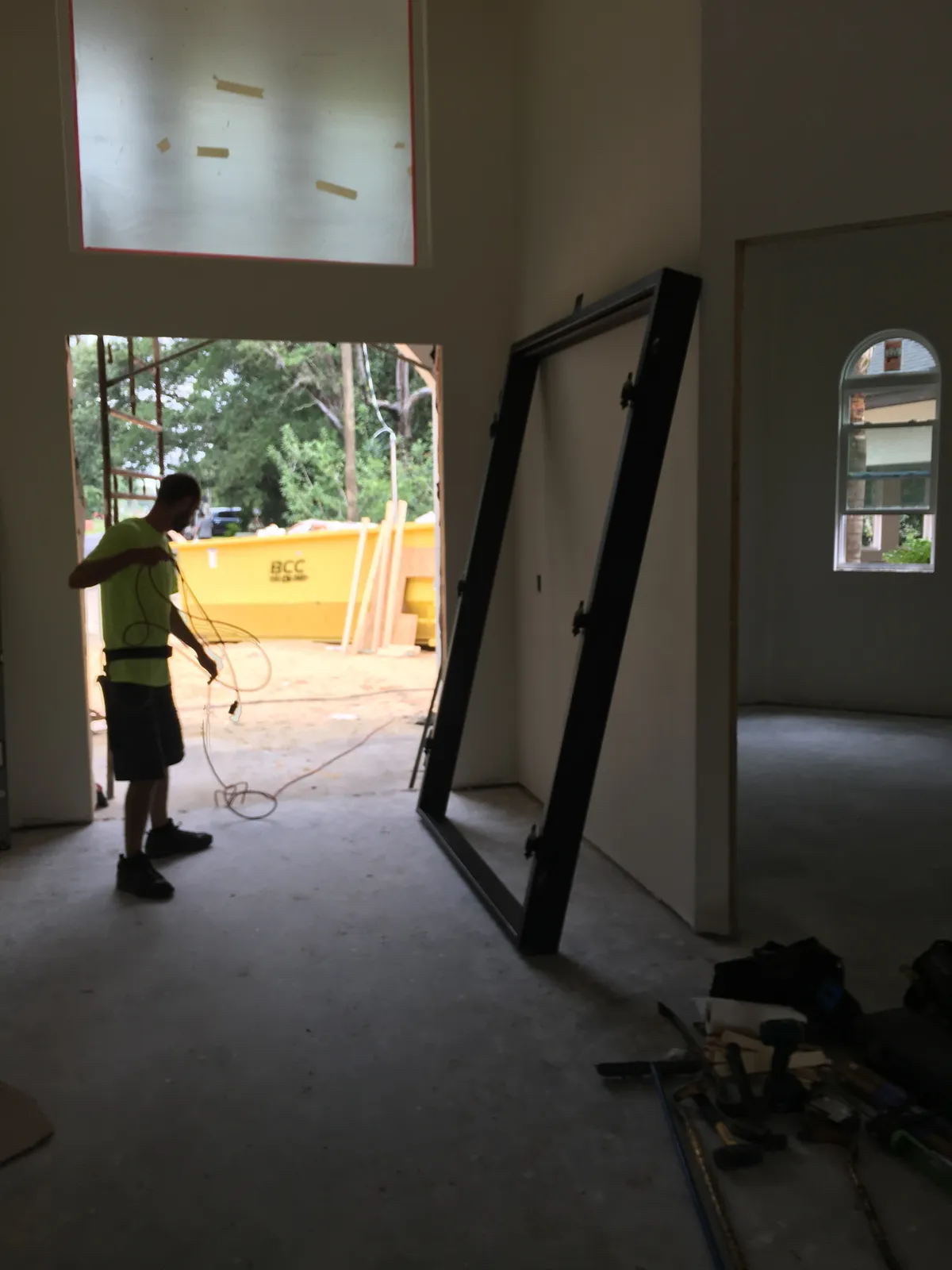 A heavy steel door frame standing at an angle inside the entry, not yet set in the opening, while a worker handles a cord nearby.