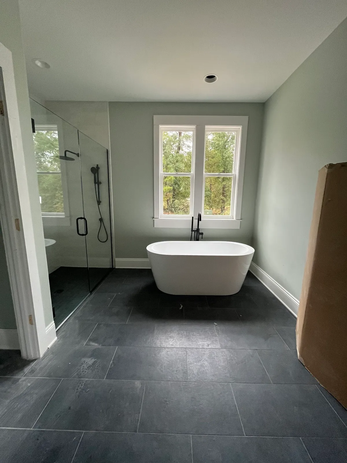 Bathroom with a freestanding tub, glass shower enclosure, and dark floor tile, with protective cardboard in the room.