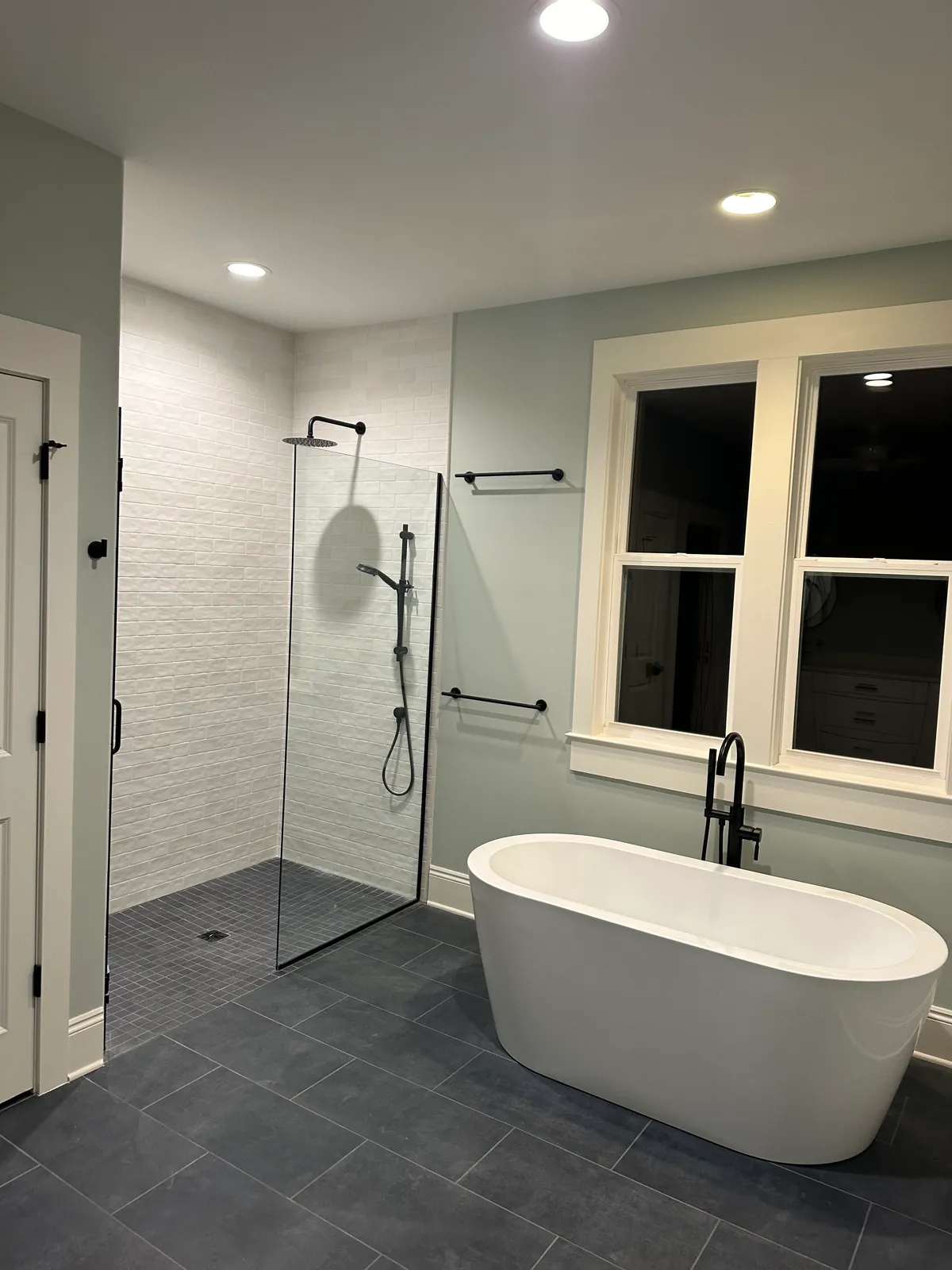 Bathroom with a freestanding tub, a glass-enclosed walk-in shower, dark floor tile, and black fixtures.