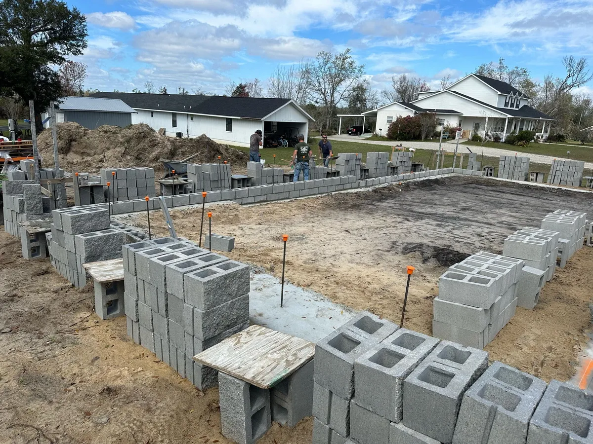 Concrete block stacked around the perimeter footing, with rebar dowels and the first courses in place.