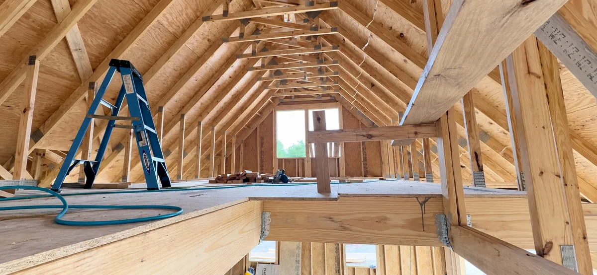 Wide view of the bonus room during construction, showing sloped roof framing, the end window, and the stair opening.