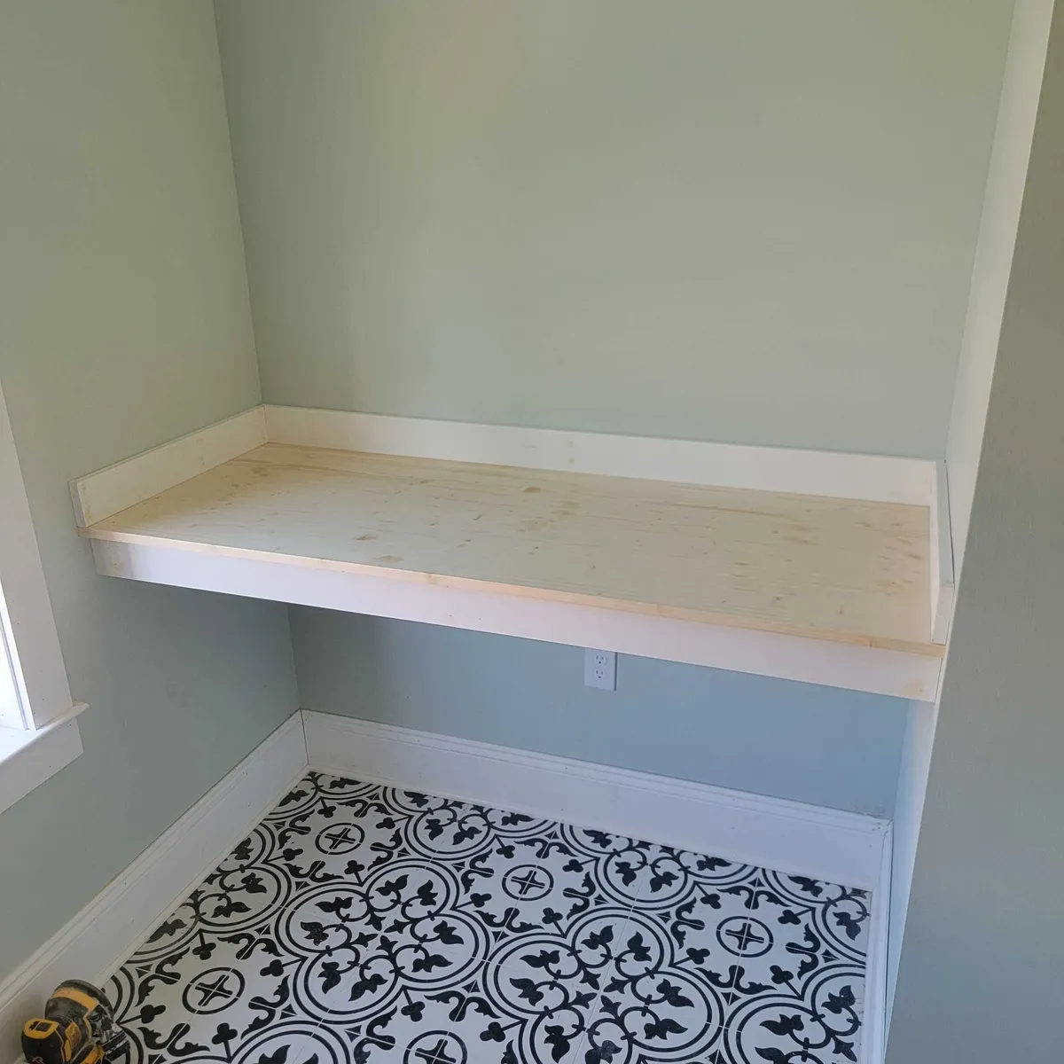 Unfinished wood built-in shelf mounted above black-and-white patterned floor tile.