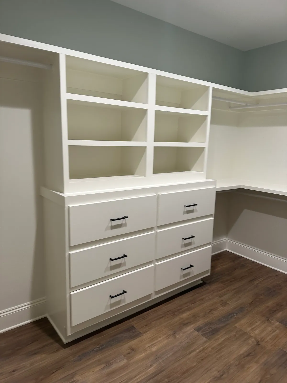 White built-in shelving above a bank of drawers, beside hanging rods.