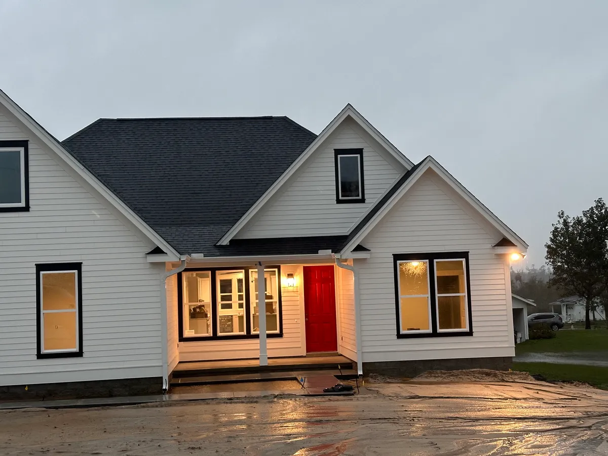 Front porch lit at dusk, with a red door and lit windows above unfinished ground.
