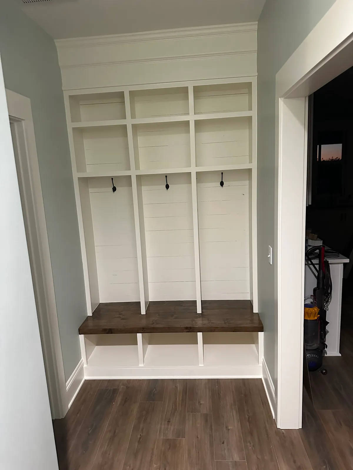 Built-in entry storage with open cubbies, hooks, and a stained wood bench.
