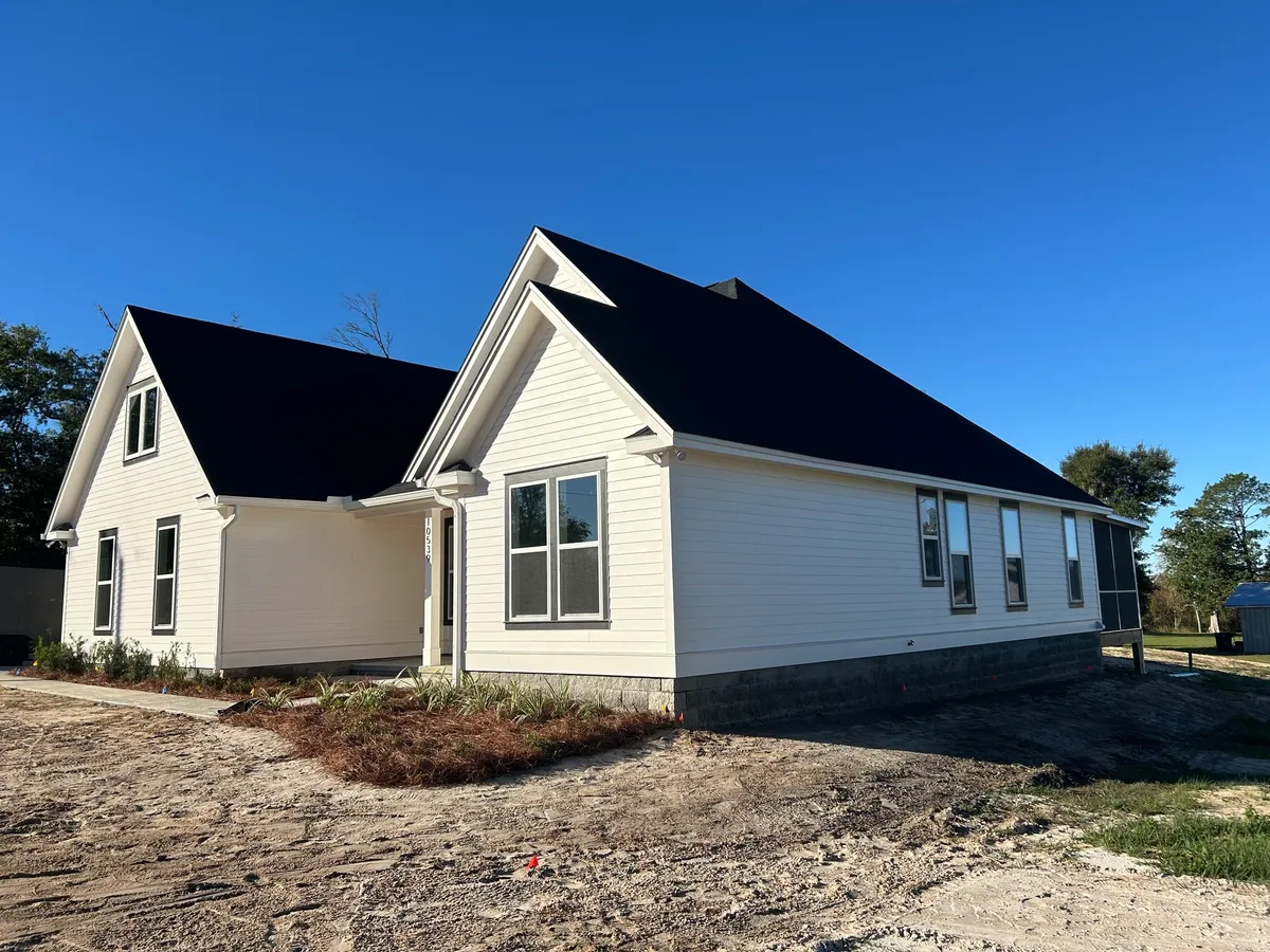 The painted house with a dark roof and new mulched planting beds, viewed across unfinished ground.