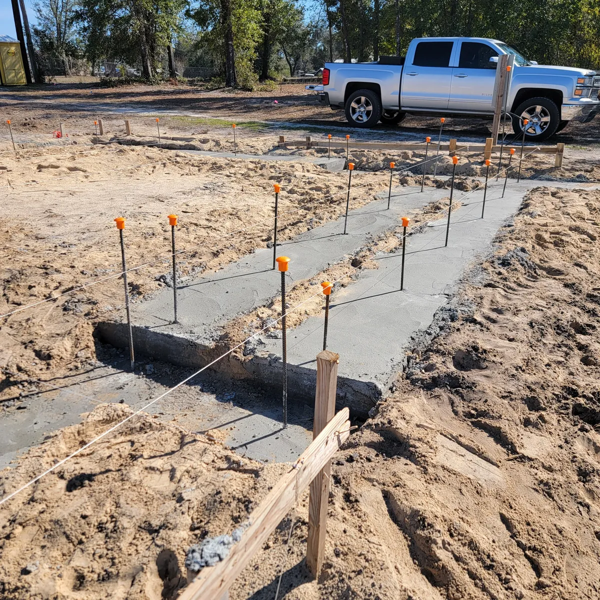 Concrete footing poured in a trench, with vertical rebar dowels capped in orange.