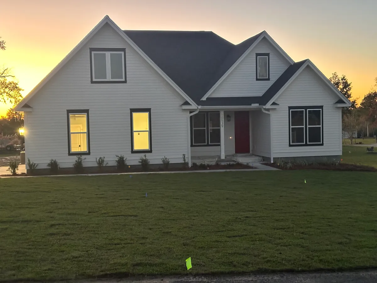 Front of the white house with lit windows and a green lawn at sunset.