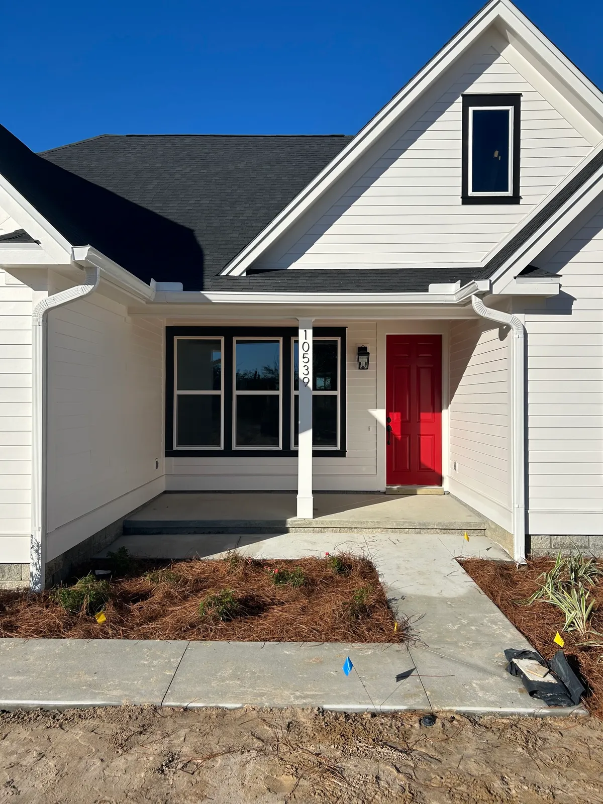 Front entry with a red door, white column, new walkway, and freshly mulched beds.