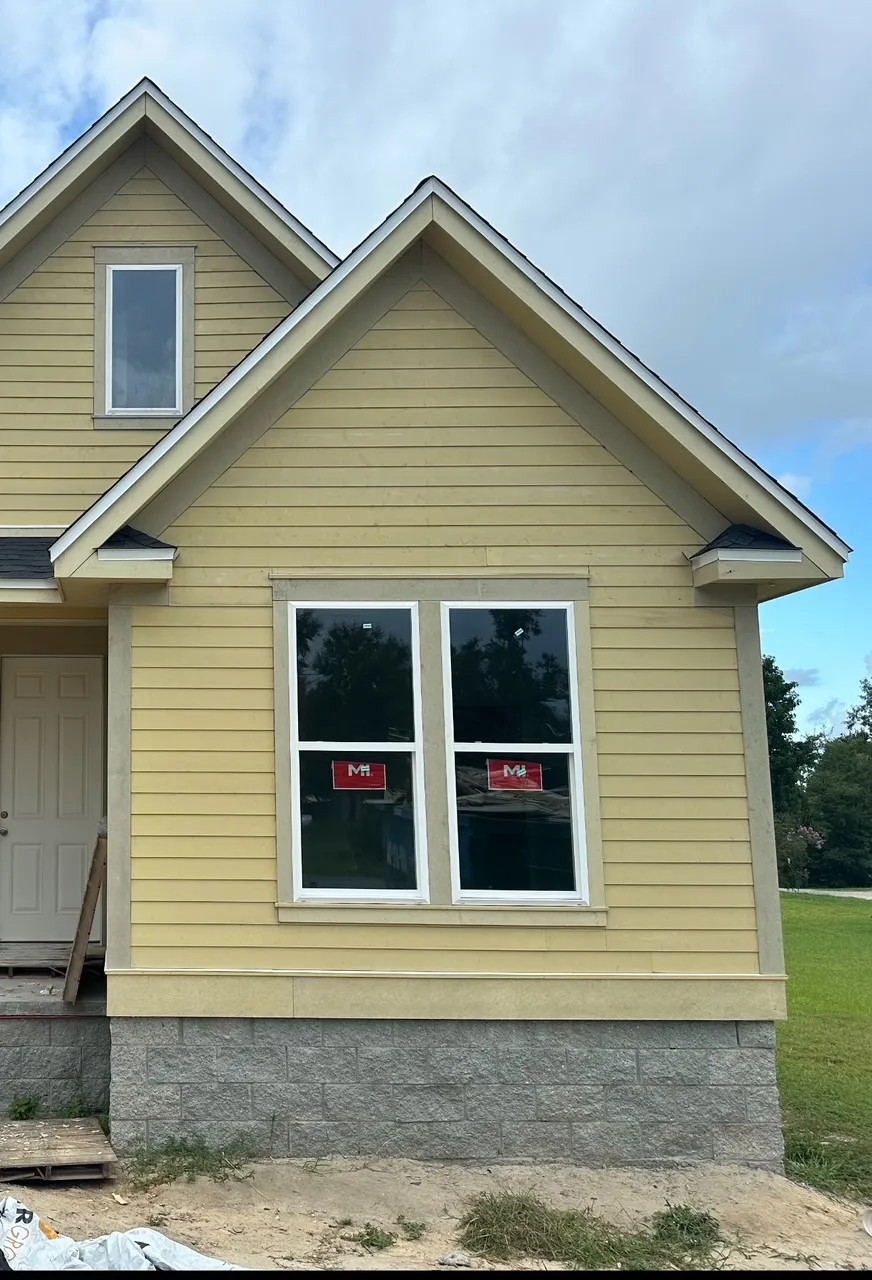 Front gables clad in unpainted yellow siding and trim, with new windows still carrying labels.