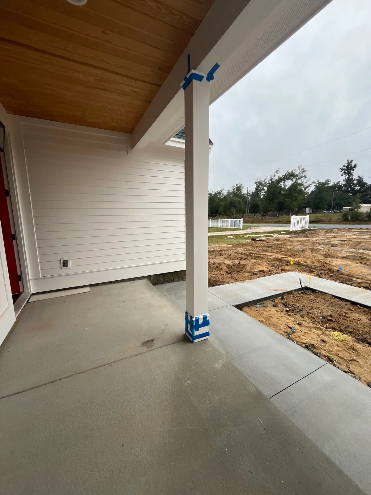 Covered porch with a white column wrapped in painter’s tape, a concrete floor, and a wood plank ceiling.
