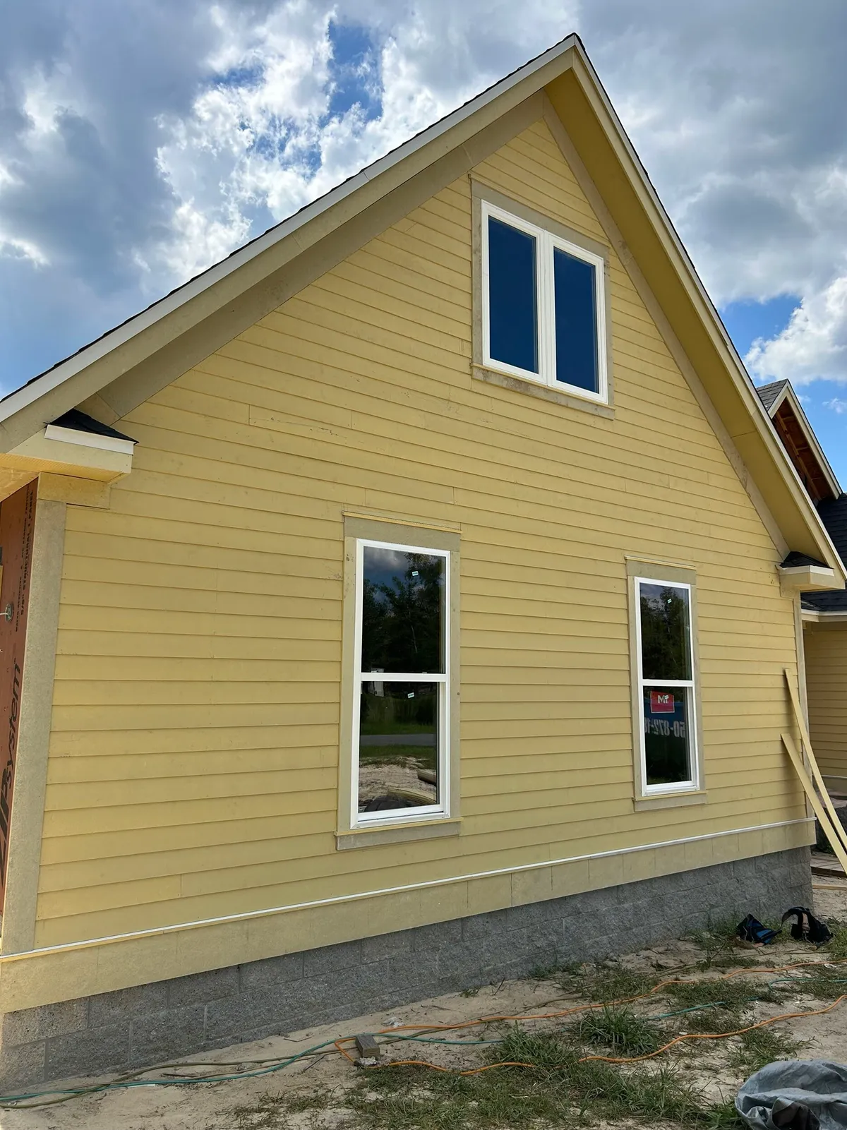 Tall gable end with unpainted yellow lap siding, trim, and windows above the stemwall.