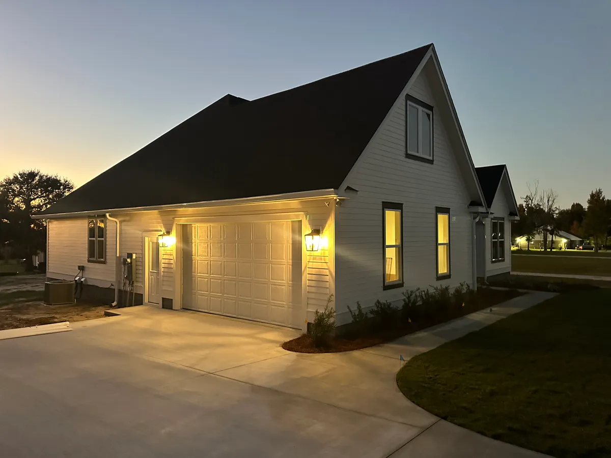 Side of the home with a lit two-car garage door and exterior lights at dusk.
