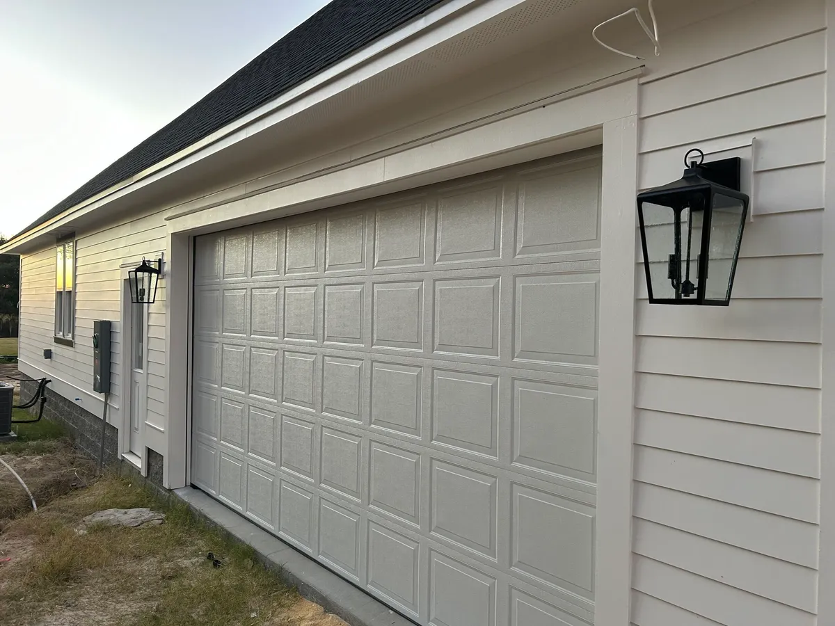 Painted siding around a paneled garage door, with a black lantern-style light.