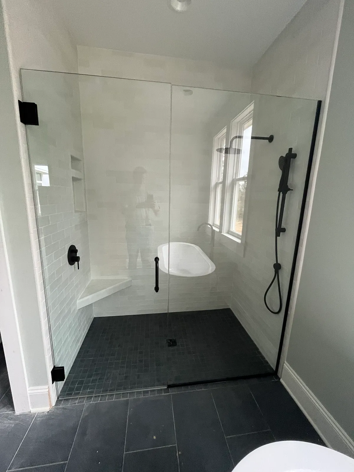 Walk-in shower with a frameless glass enclosure, light wall tile, dark floor tile, and black fixtures.