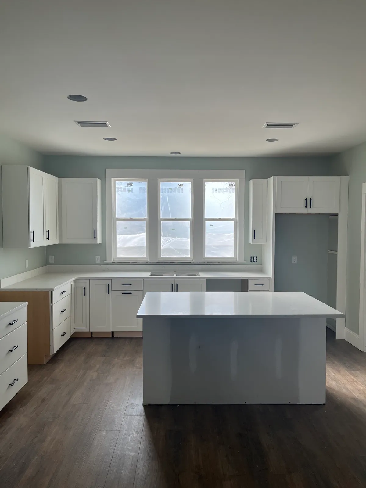 Kitchen with white shaker cabinets, light counters, and an island, with appliance spaces still empty.