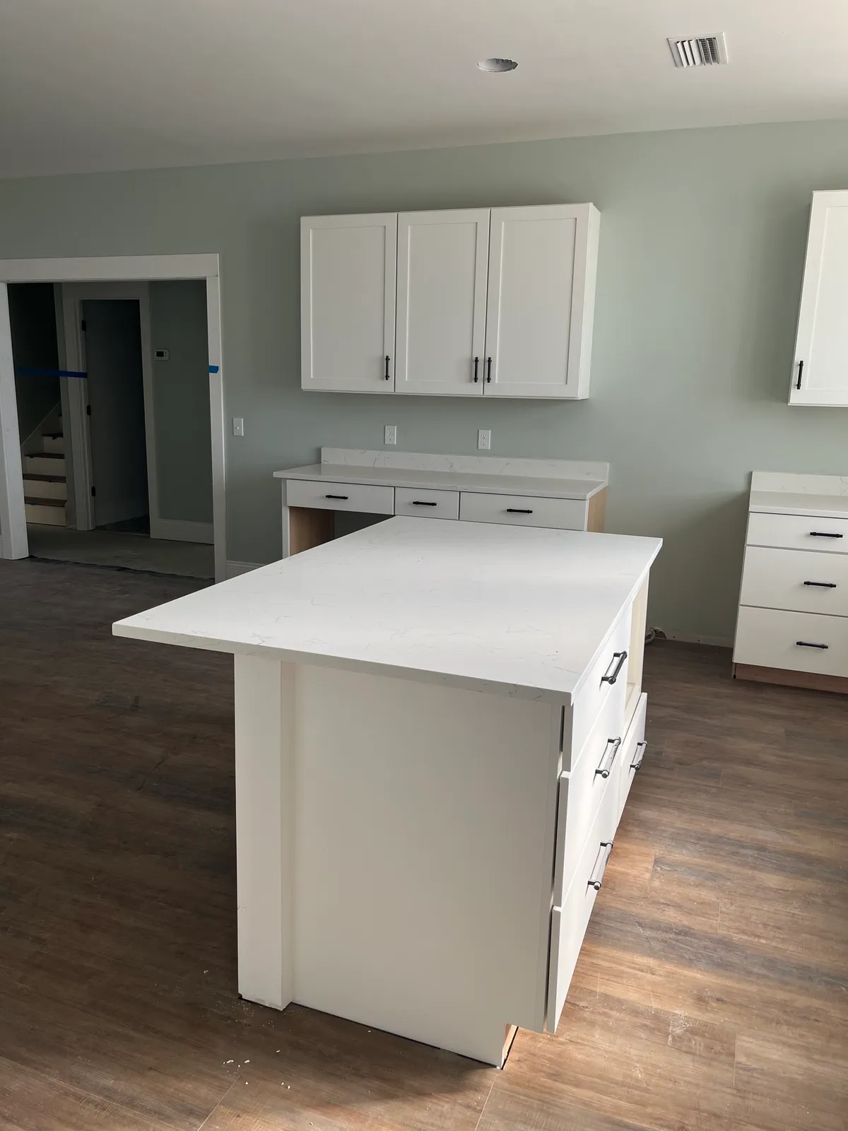 Kitchen island with white cabinets and counter, with a doorway and stair visible beyond.