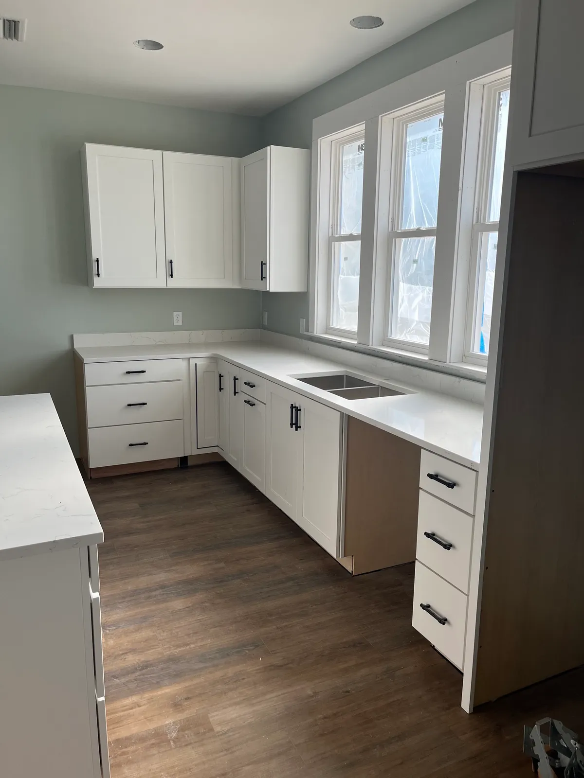 Corner of the kitchen cabinetry with an undermount sink and no faucet installed, beside a window wall.