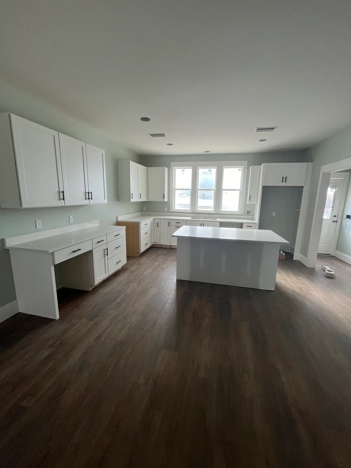 Wide view of the kitchen with perimeter cabinets, an island, and a cabinet run with knee space.