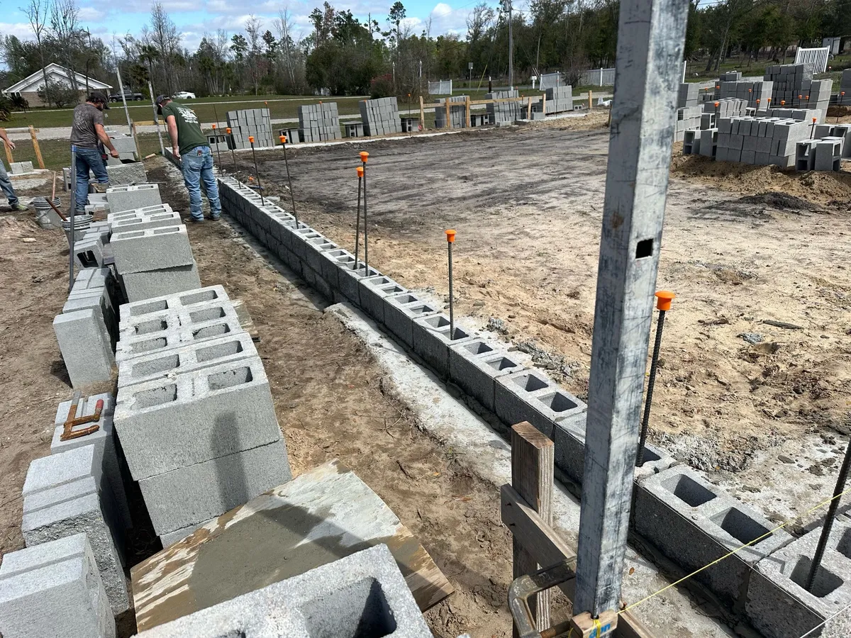 Crew members laying concrete block along the footing, with rebar dowels and stacked block nearby.