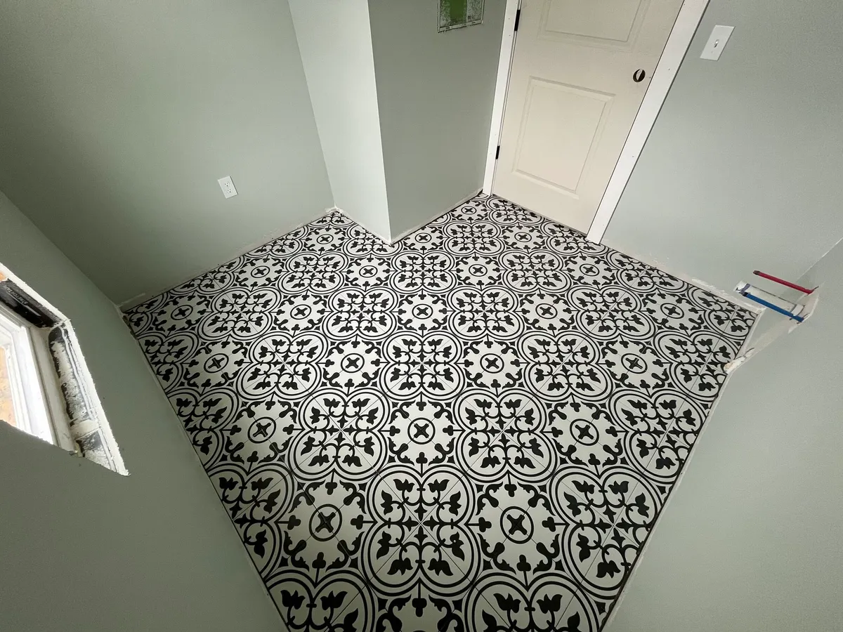 Overhead view of black-and-white patterned floor tile in a small room with a door and window.