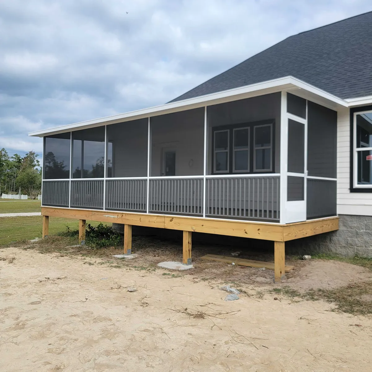 Screened rear porch on wood posts above bare ground, before skirting and landscaping.