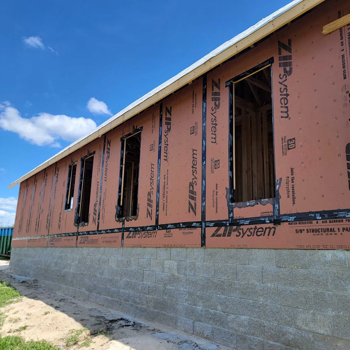 Side wall sheathed in ZIP System panels with framed window openings above the split-face stemwall.