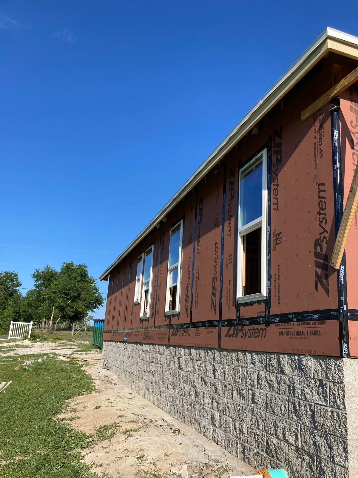 Side of the house in ZIP System sheathing with installed windows above the split-face stemwall.