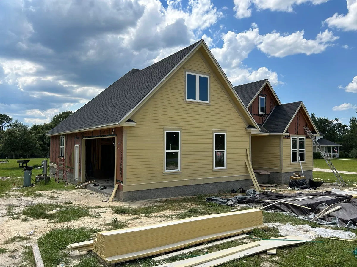 Garage end of the house clad in unpainted yellow lap siding, with siding materials on the ground.